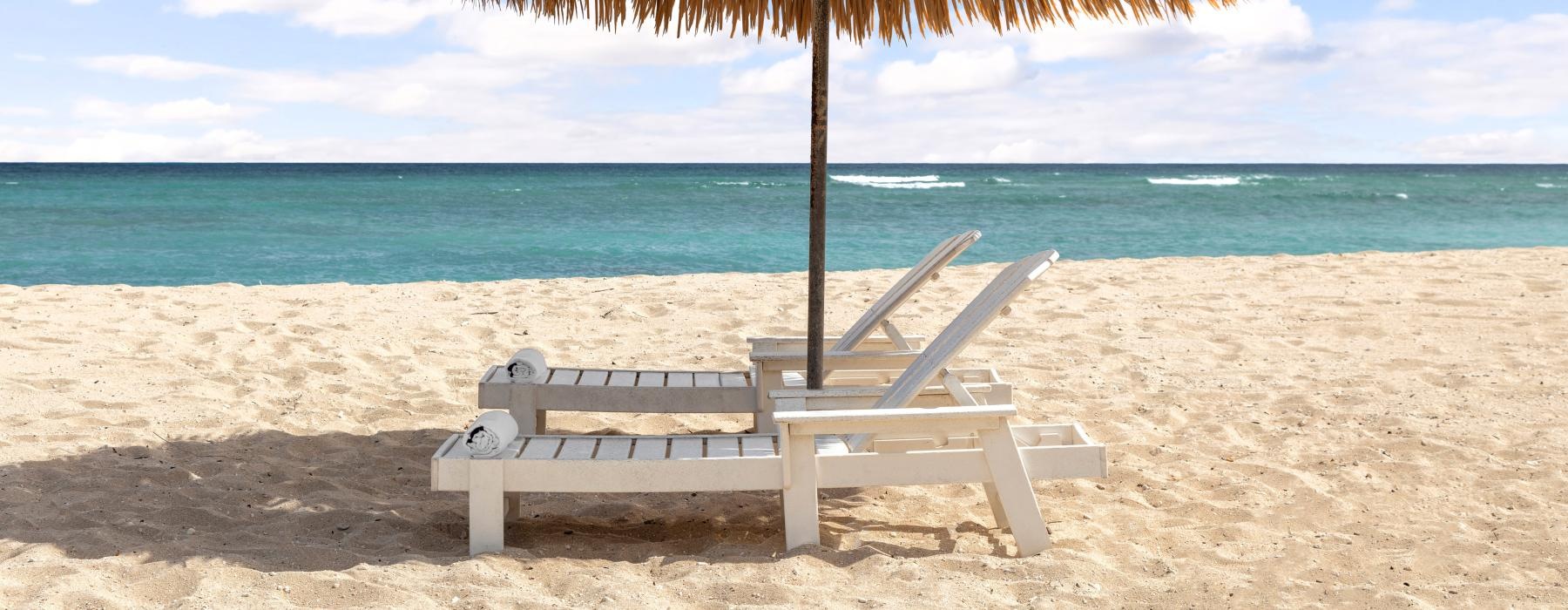 lounge chairs under an umbrella on a beach